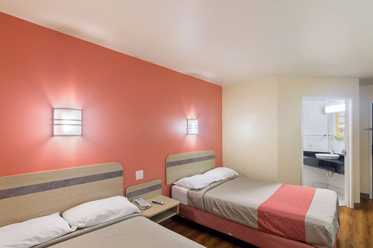 Una habitación de hotel con dos camas, un baño con lavamanos y un espejo.