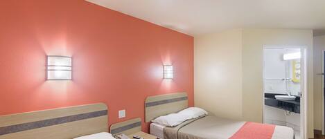 A hotel room with two beds, a bathroom with a sink, and a mirror.