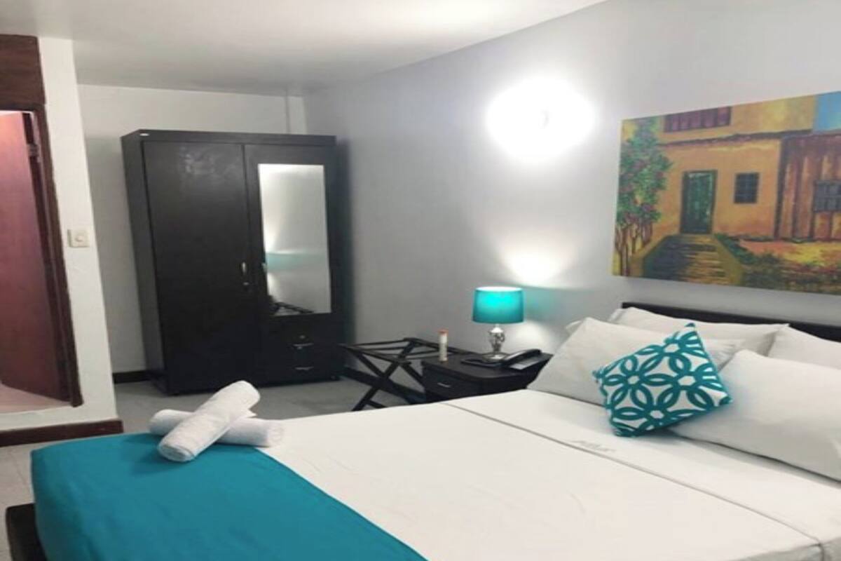 A hotel room with a bed, a desk, a chair, a wardrobe, and a painting on the wall.
