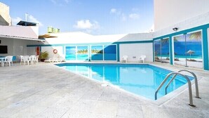 Una piscina con agua cristalina azul, rodeada de sillas de descanso blancas y un suelo de baldosas.