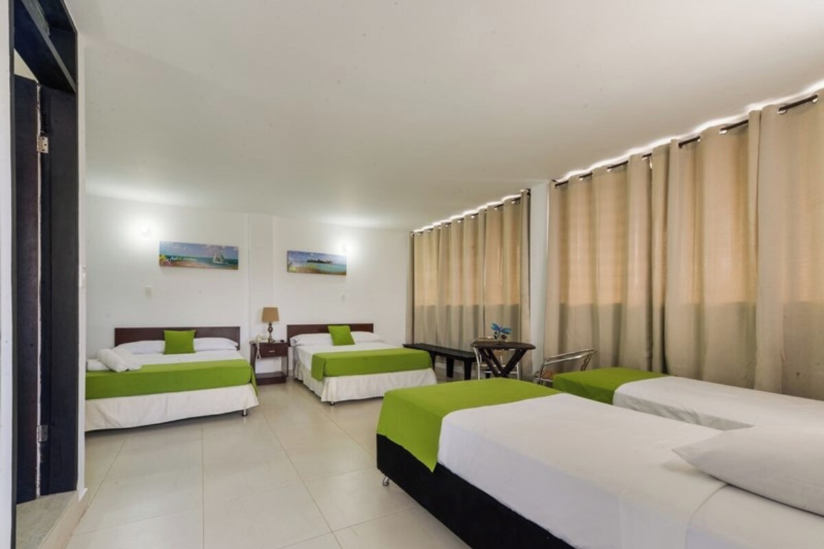 A hotel room with three beds, a desk, and a chair. There are two paintings on the wall.