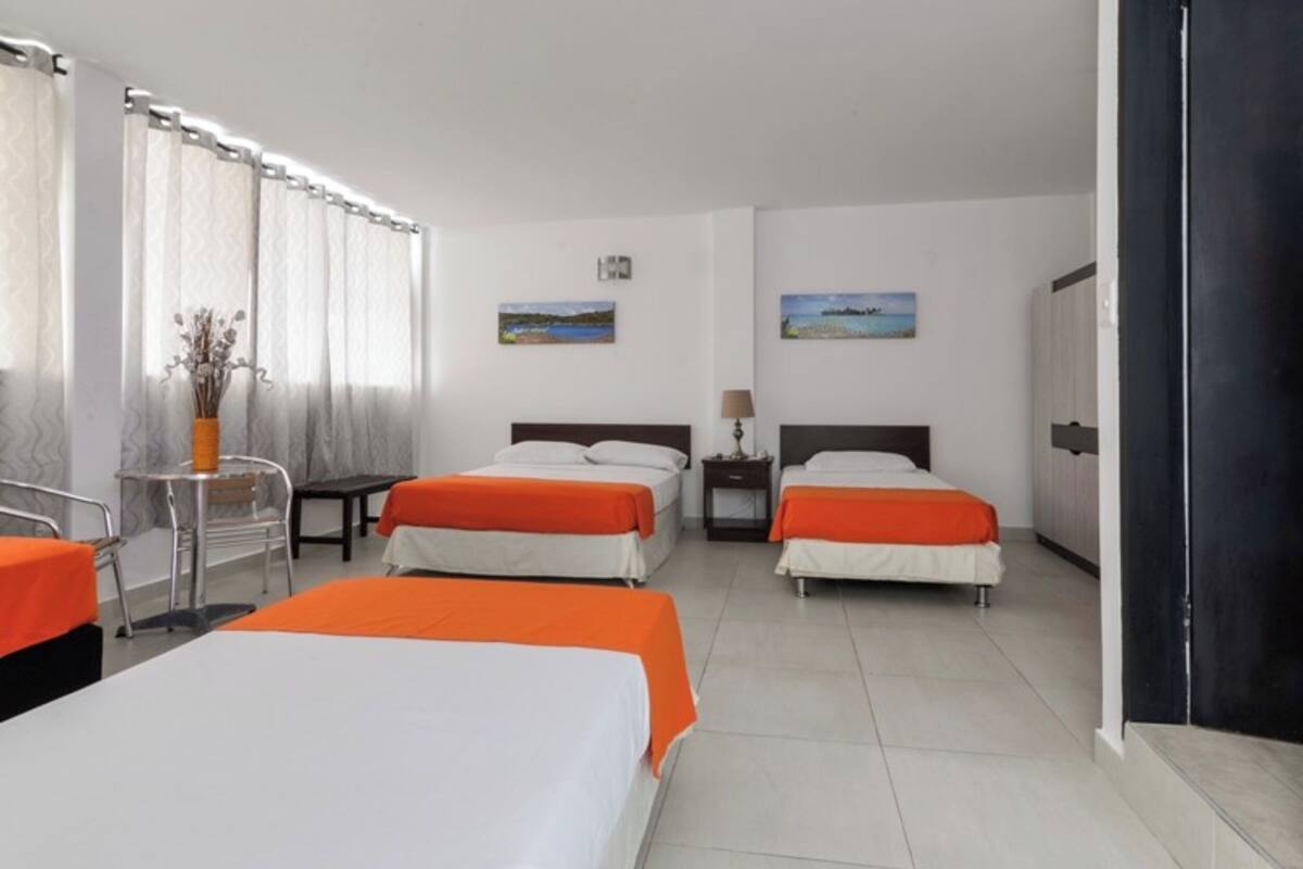 A hotel room with three beds, a desk, a chair, and a window with curtains.
