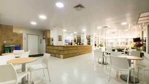 Un vestíbulo de hotel con mostrador de recepción, sillas y mesas blancas.