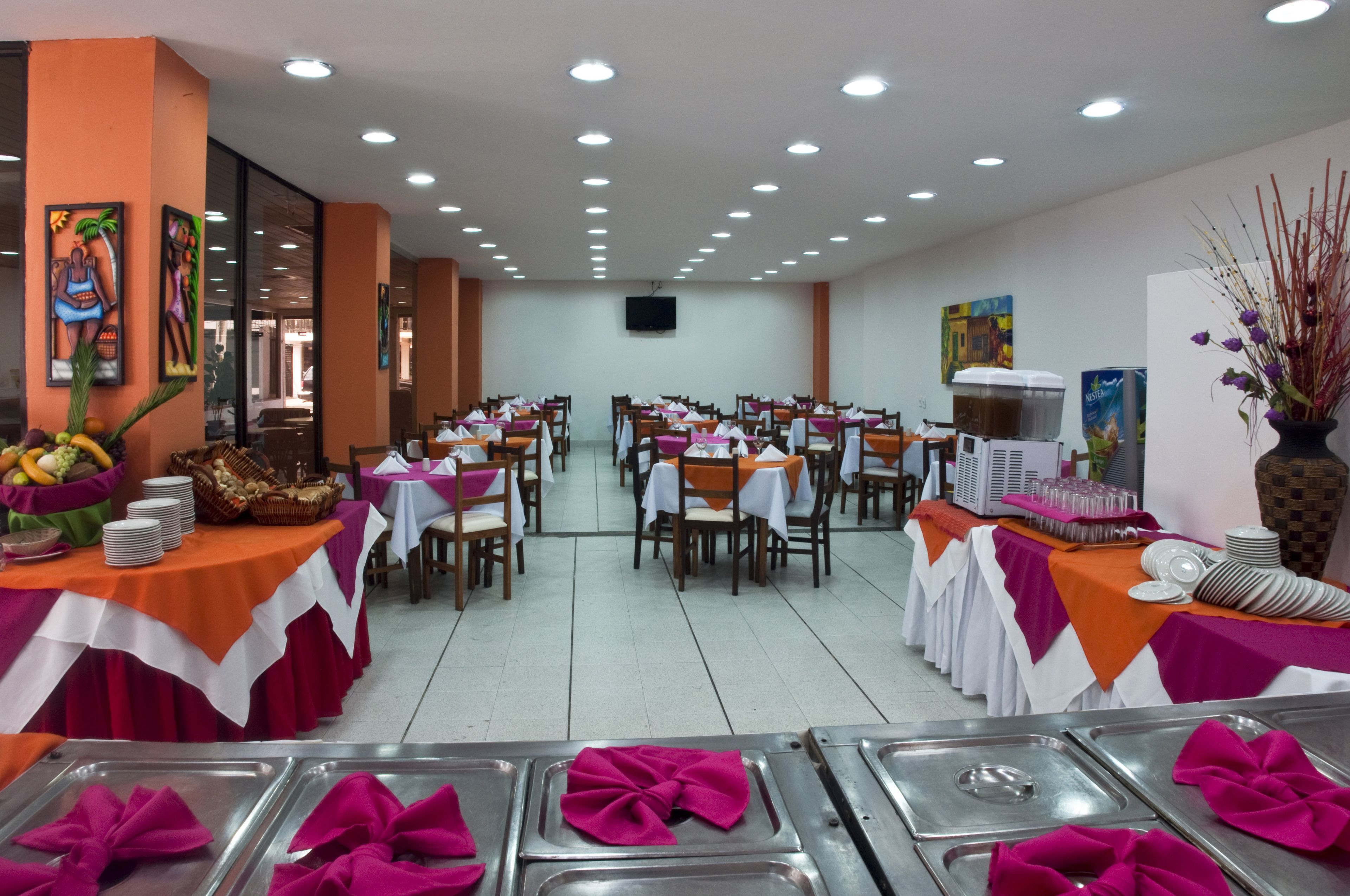 A spacious dining area with multiple tables and chairs, a buffet setup, and artwork on the walls.