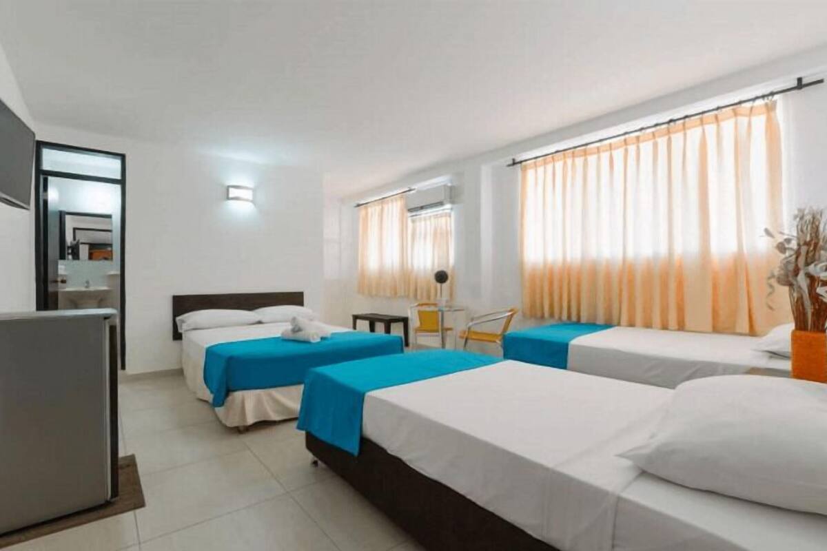 A hotel room with two beds, a desk, a chair, a TV, and a window with curtains.