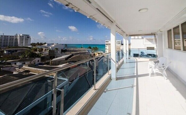 A balcony with a glass railing overlooking a coastal area with buildings and a clear sky. - Hotel Verde Mar (San Andrés)