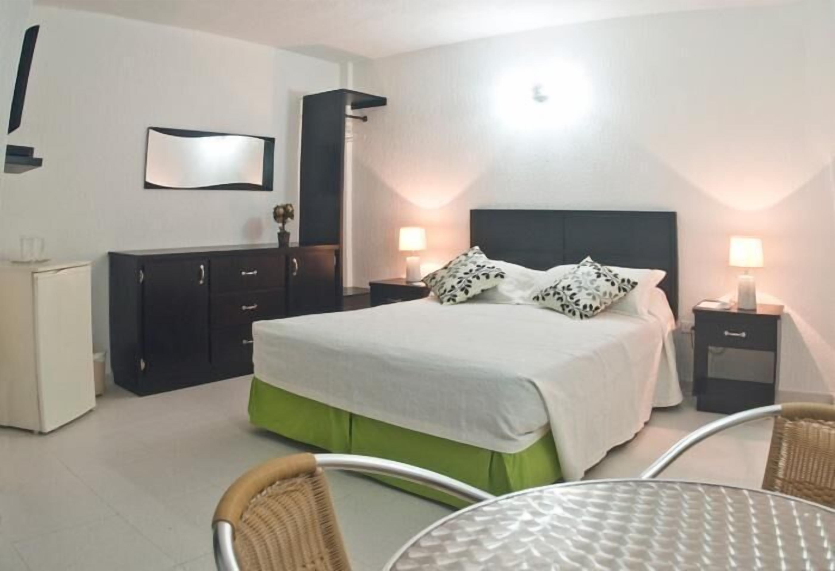A bedroom with a bed, bedside tables, a wardrobe, and a dining area with chairs and a table.