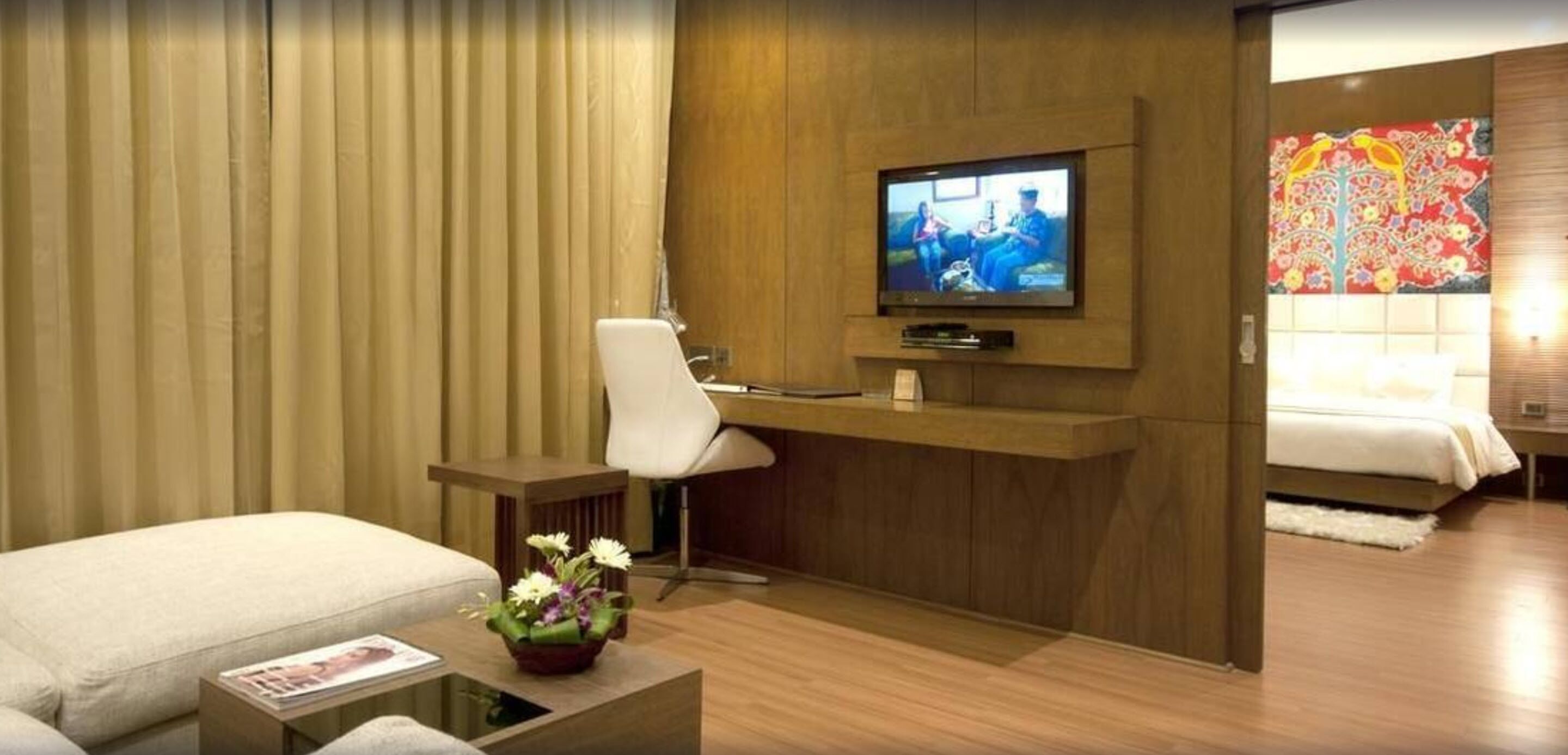 A hotel room with a bed, a desk with a chair, a television, and a decorative wall piece.