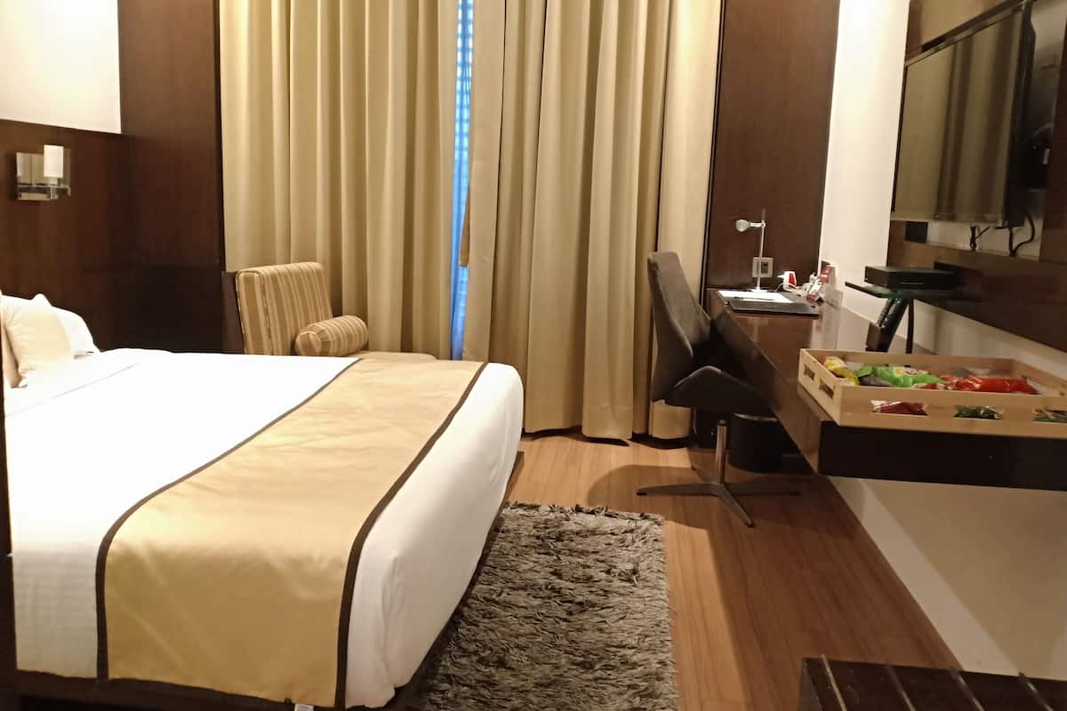 Habitación de hotel con una cama grande, un escritorio, una silla, un espejo y una ventana con cortinas.
