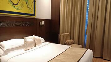 A hotel room with a large bed, a headboard with a wavy design, a wall-mounted light fixture, and a window with curtains.