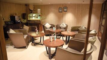 A hotel lobby with round tables and chairs, a reception desk, and a display case with items.