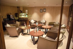 A hotel lobby with round tables and chairs, a reception desk, and a display case with items.