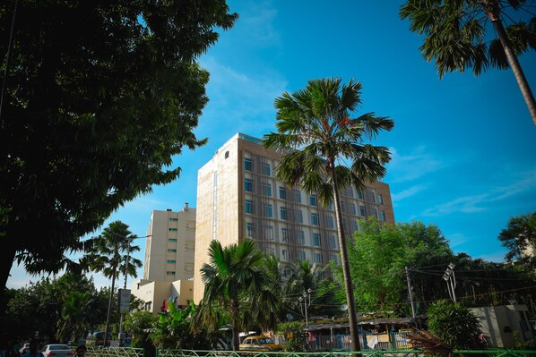 Un edificio de varios pisos con un diseño arquitectónico moderno, rodeado de abundante vegetación y palmeras.