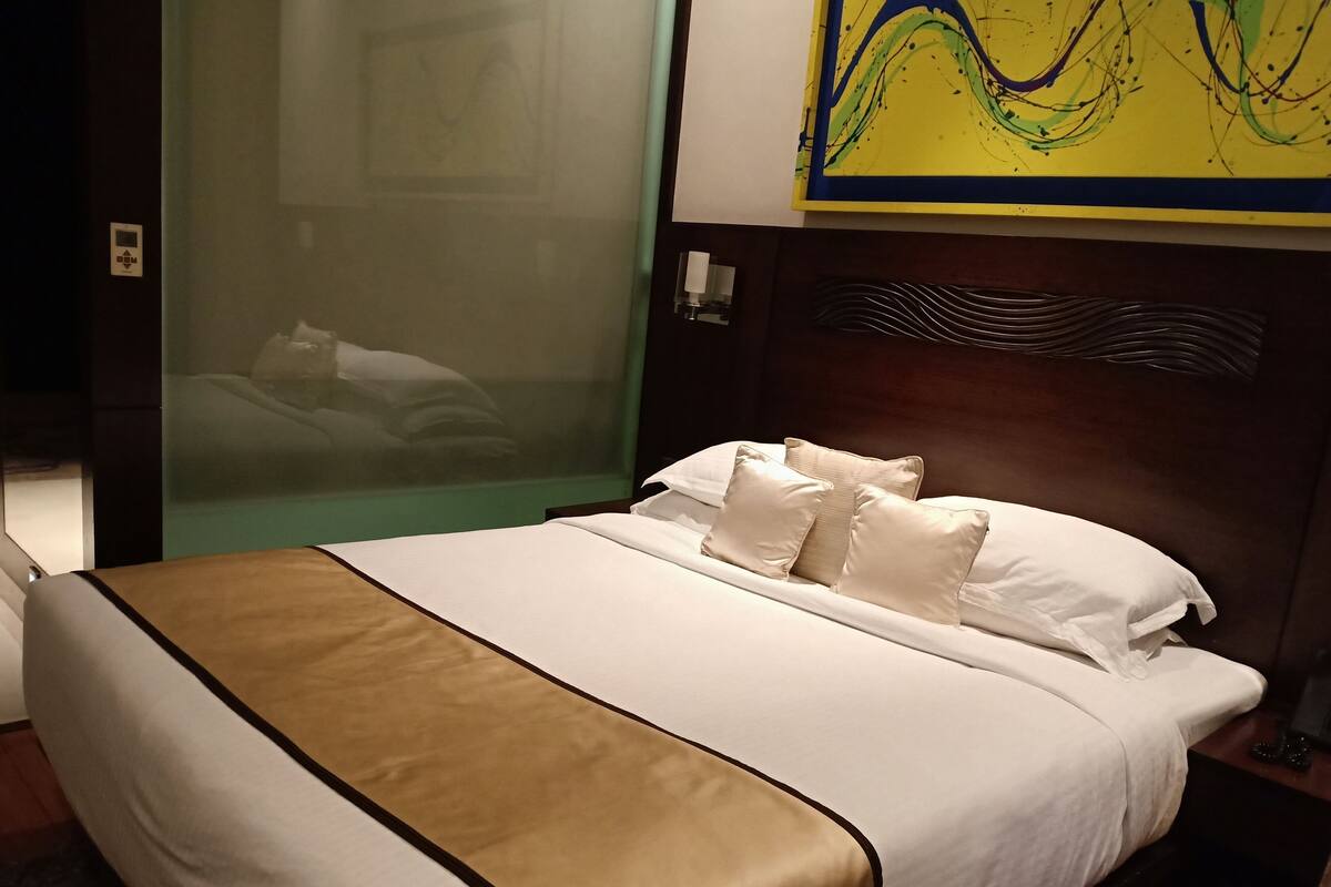 Habitación de hotel con cama, mesita de noche, cuadro en la pared y ventana con vistas.