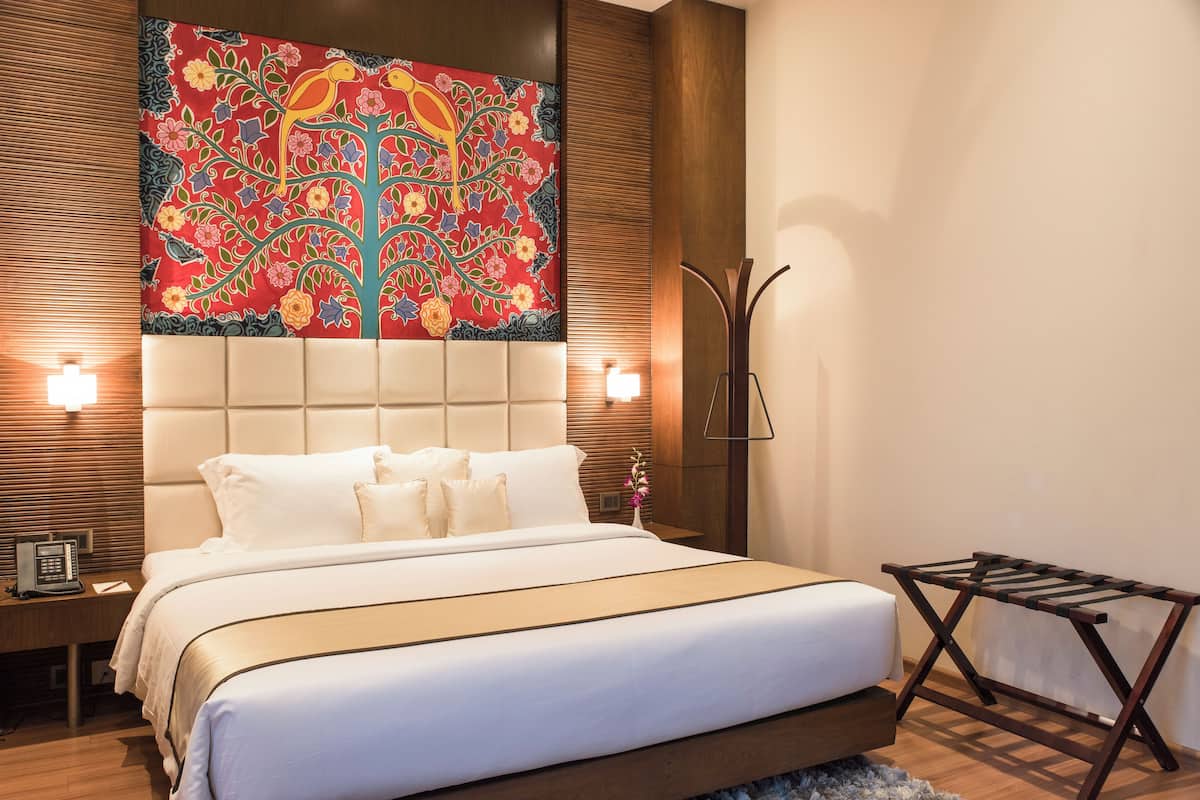 Habitación de hotel con una cama grande, cabecera de madera, un tapiz colorido y una mesita de noche pequeña con un teléfono.