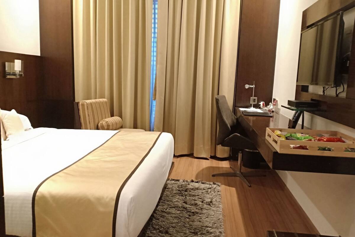 Habitación de hotel con cama, escritorio, silla, espejo y ventana con cortinas.
