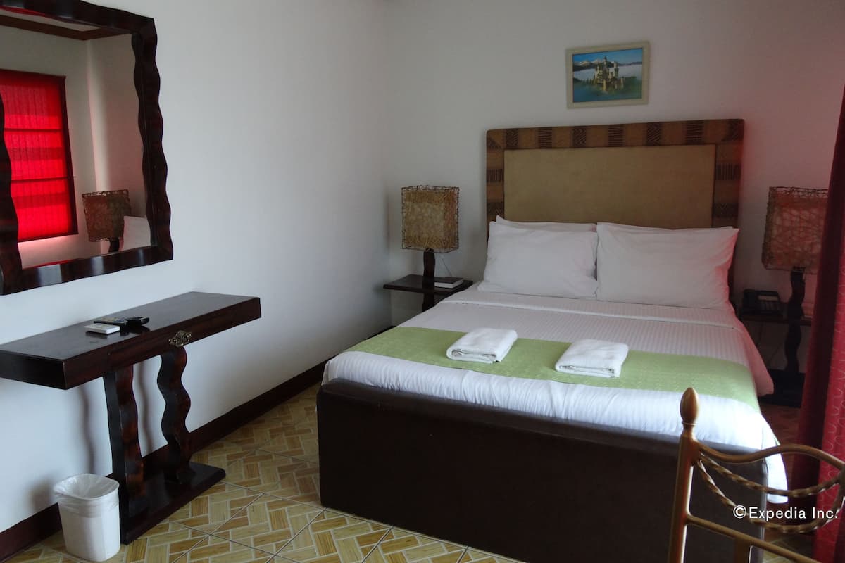 A hotel room with a bed, a nightstand, a bedside table, a chair, a trash bin, and a mirror.