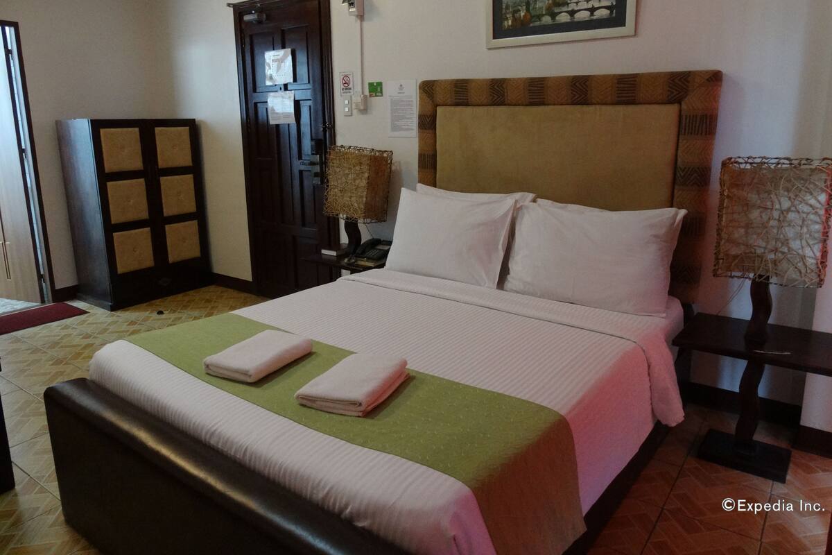 A hotel room with a large bed, a desk, a chair, a lamp, and a door.