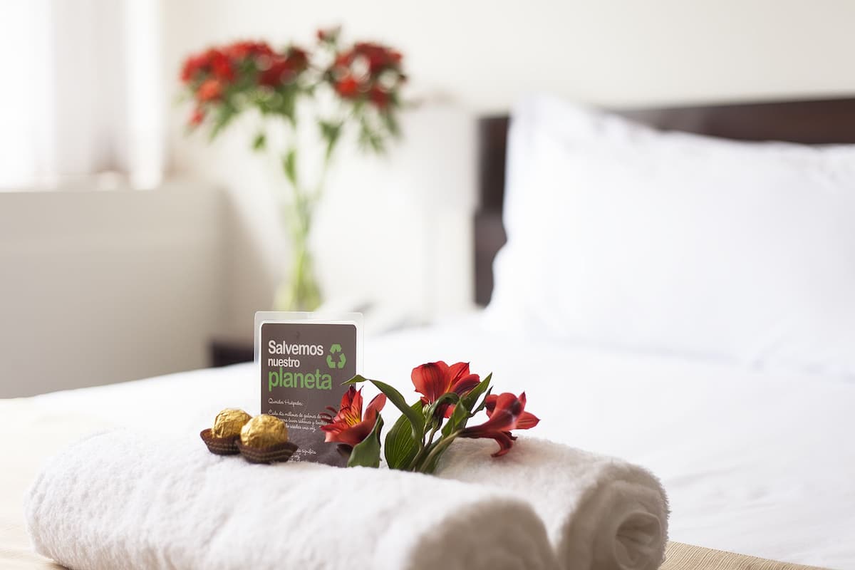 Una cama bien hecha con una toalla blanca, una tarjeta y un ramo de flores rojas.