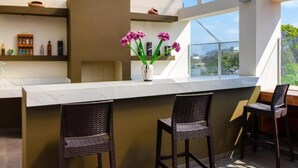 Une cuisine moderne avec un plan de travail en marbre, des tabourets de bar en osier et un vase rempli de fleurs violettes.
