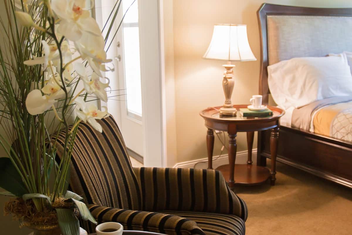 A hotel room with a bed, a striped sofa, a small table with a coffee cup, a plate of cookies, and a vase of white orchids.