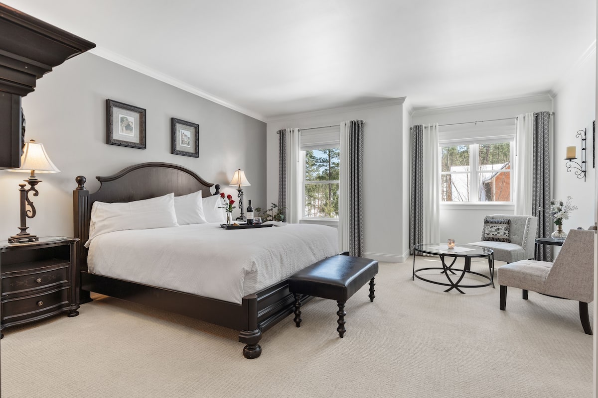 A bedroom with a large bed, bedside tables with lamps, a bench, a chair, and a small table.