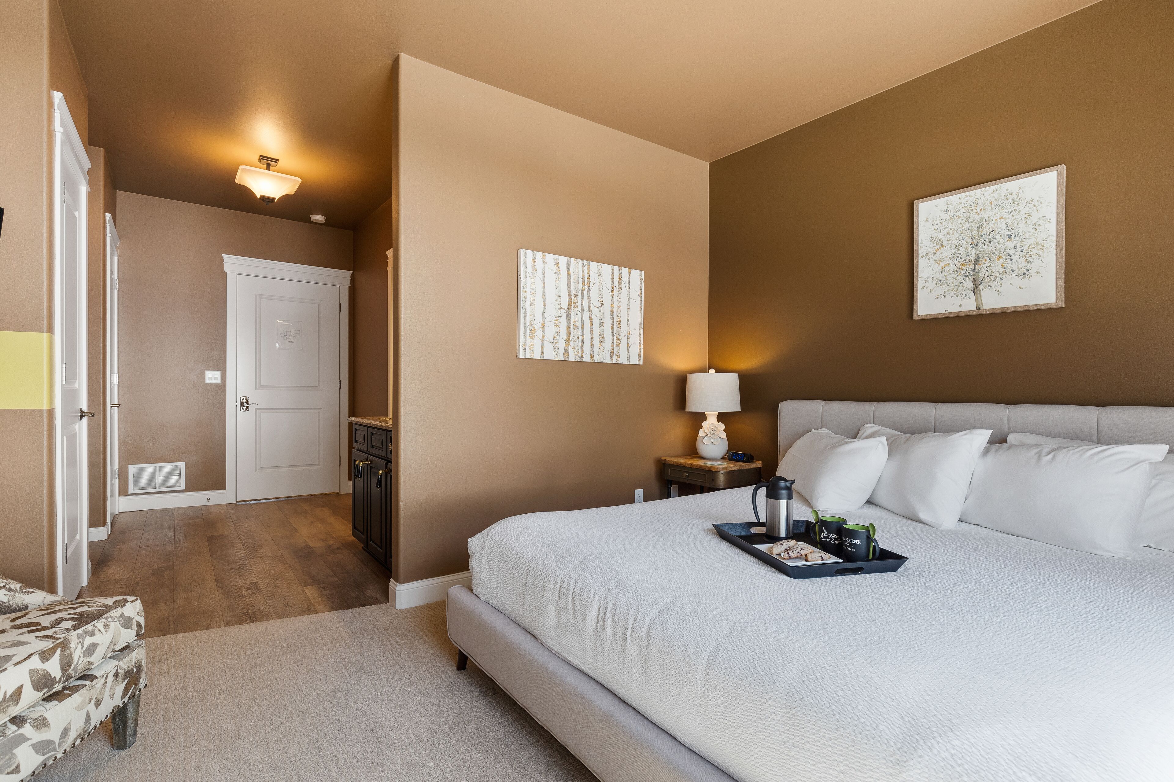 A bedroom with a large bed, a nightstand with a lamp, and a tray with items on it.