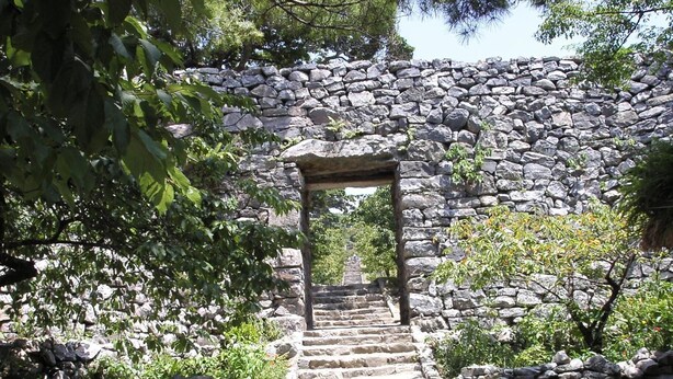 Un escalier en pierre mène à une arche en pierre, elle-même entourée de verdure.