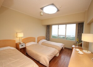 A hotel room with three beds, a large window, and a view of the cityscape.