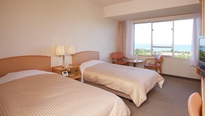 Une chambre d’hôtel avec deux lits, un bureau avec une lampe, une chaise, une télévision et une grande fenêtre donnant sur la mer.
