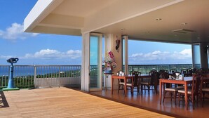 Un vaste espace extérieur aménagé pour les repas, avec une terrasse en bois, une table dressée pour quatre personnes et une vue sur l’océan.