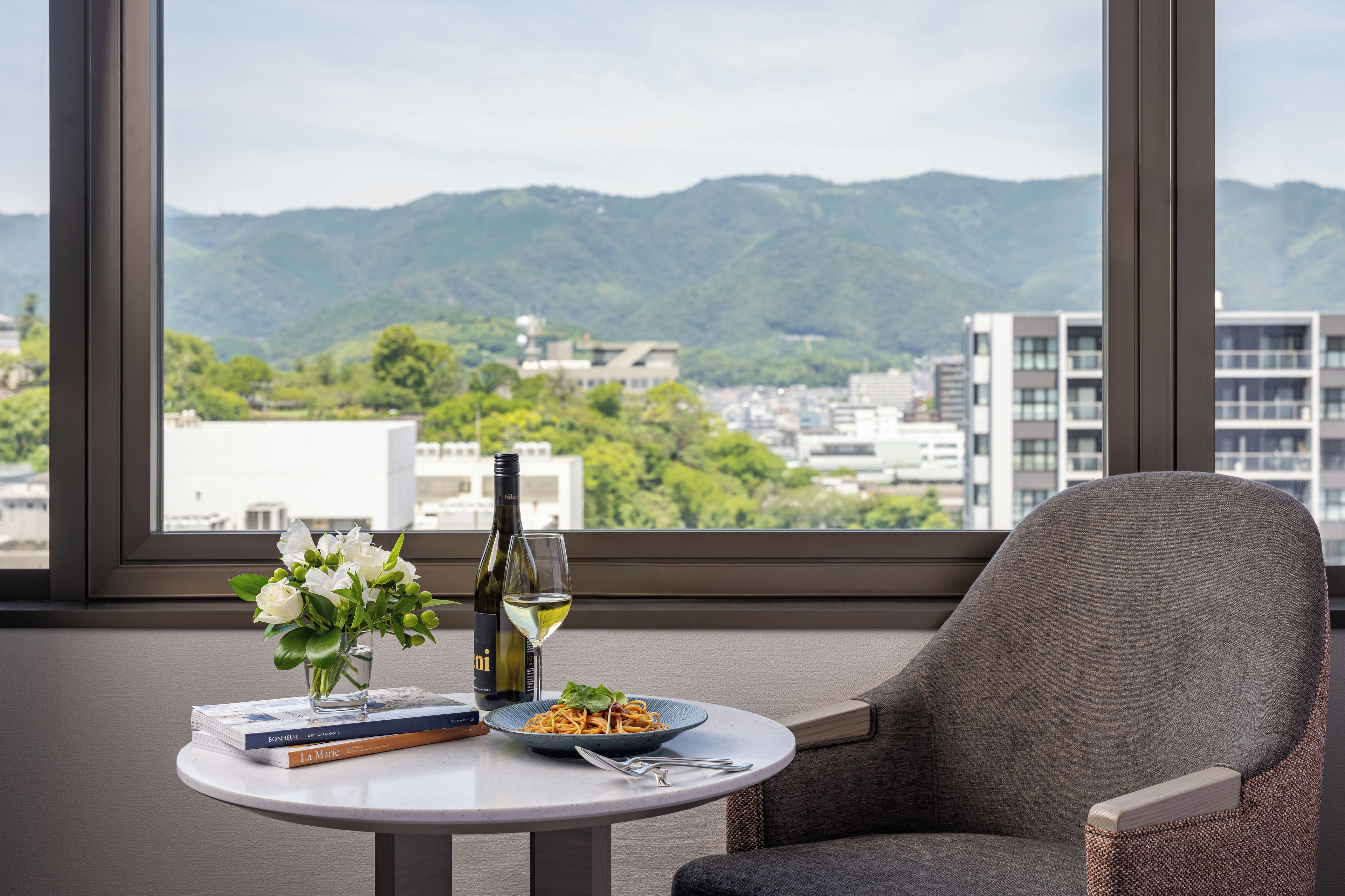 Una habitación con vista a las montañas, una mesa con una botella de vino, una copa y un plato de comida.