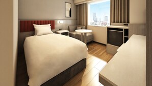 Een hotelkamer met een bed, nachtkastjes, een bureau, een stoel, een klein rond tafeltje, een televisie en een raam met uitzicht op de stad.
