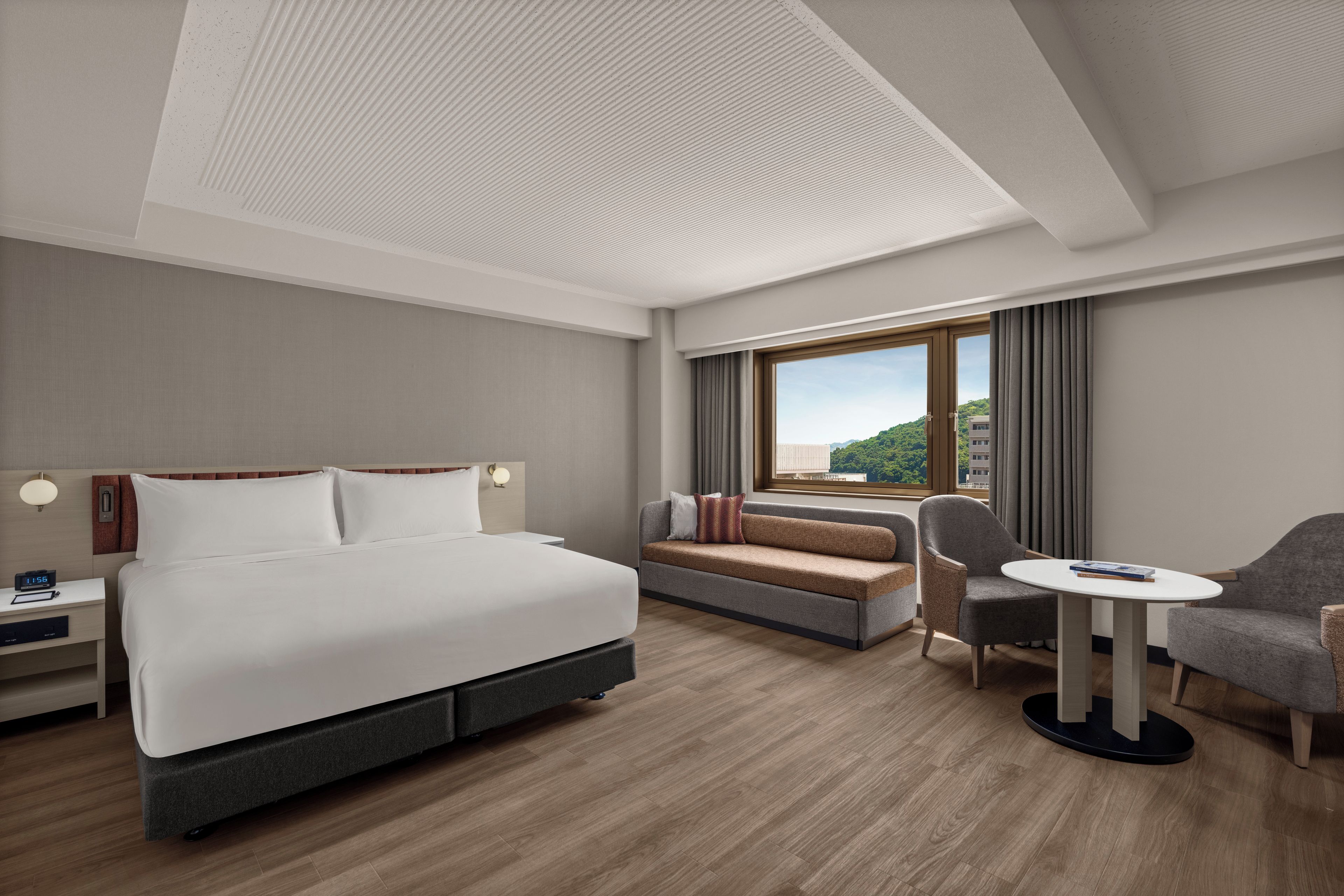 Habitación de hotel con cama, sofá, sillón, una mesita y ventana con vistas.
