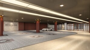 A modern building entrance with a white car parked inside, large pillars, and a sign reading 'ANA CROWNE PLAZA BY IHG.'