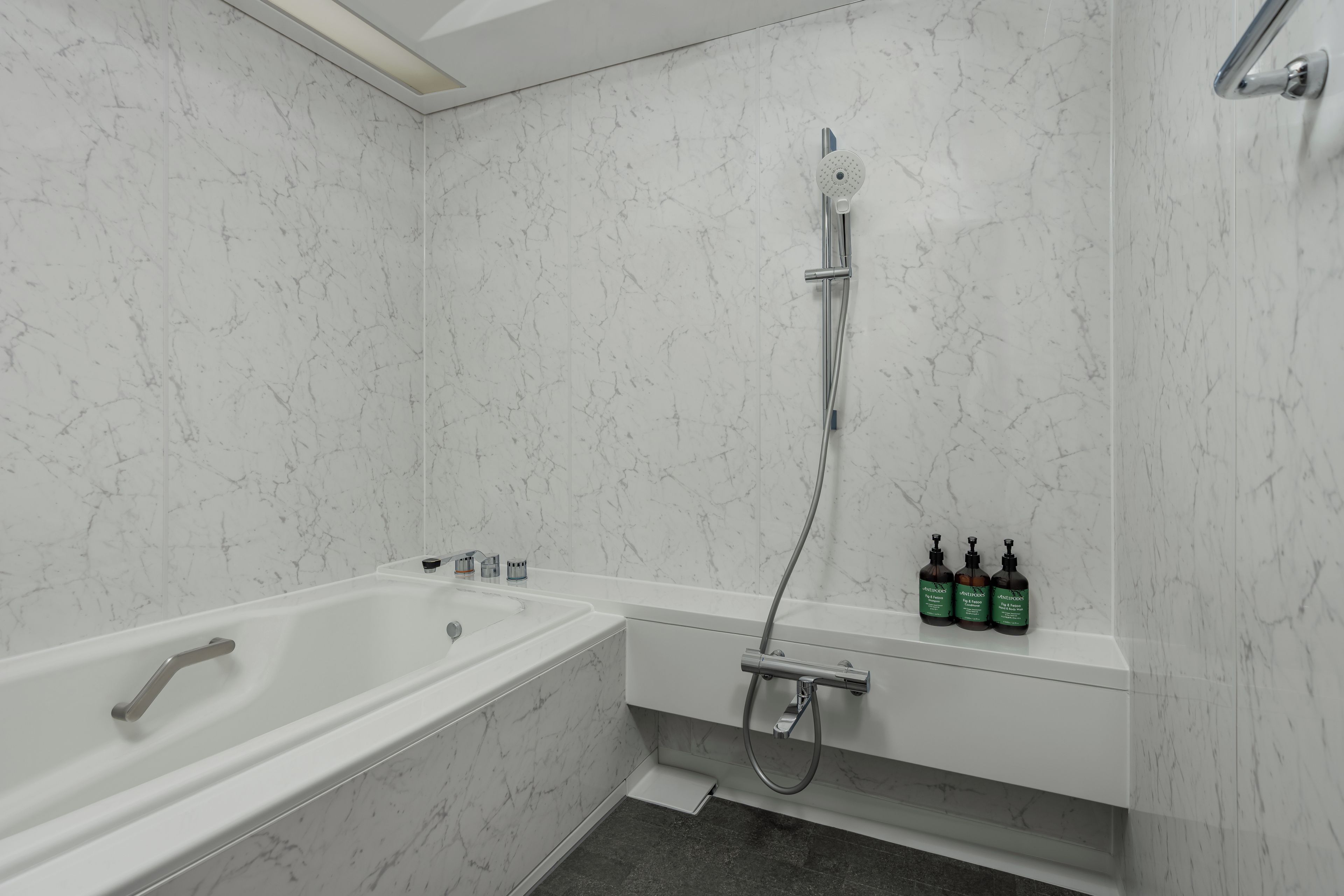 A bathroom with a white marble wall, a bathtub, a shower, and a shelf with three bottles.