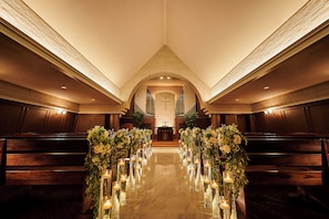 Eine Seitenbankreihe, eine mittlere Bankgasse mit Blumenarrangements und Kerzen, und Blick zum Altar am Ende.