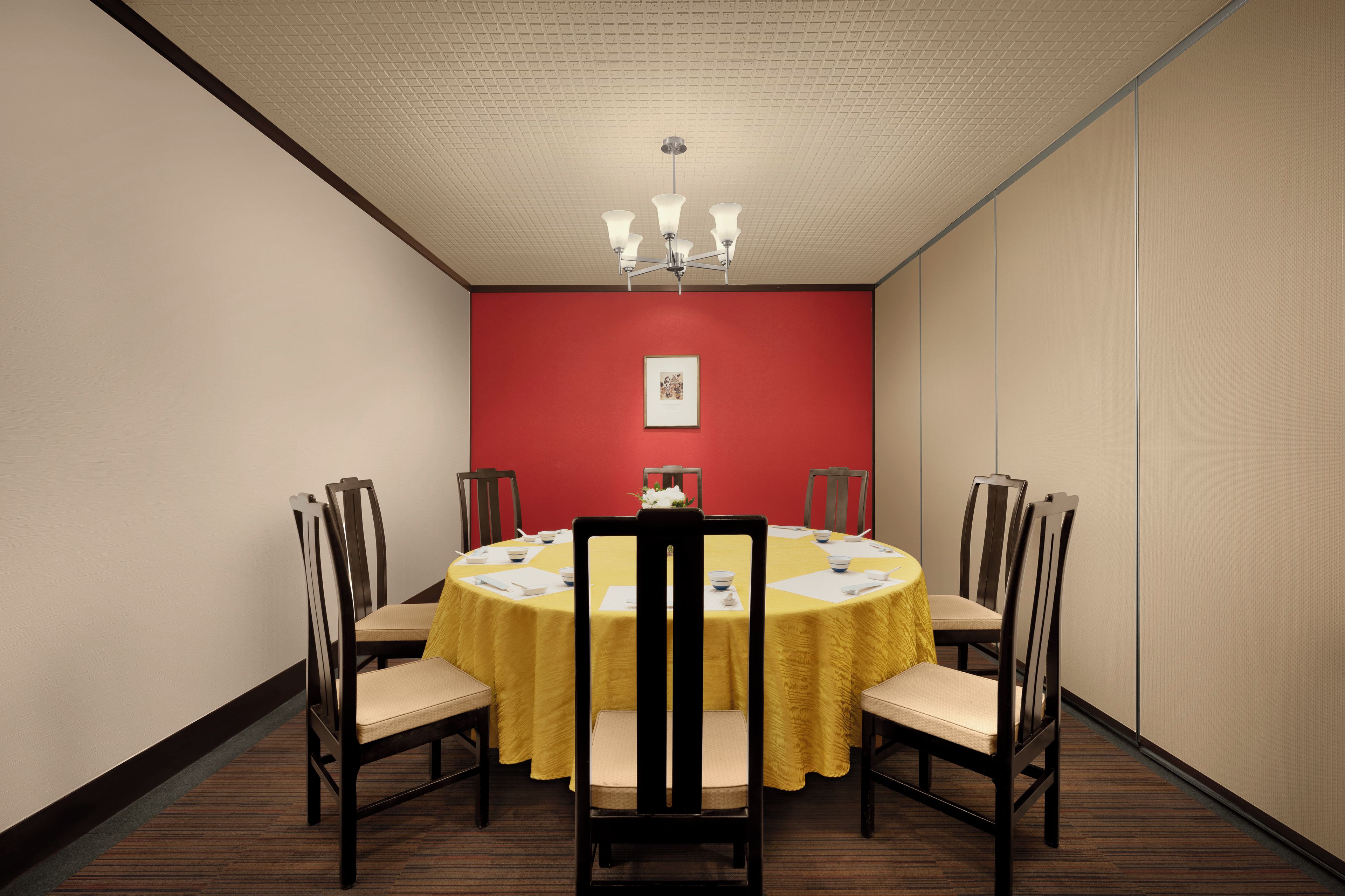 A conference room with a round table, chairs, a chandelier, and a red accent wall.