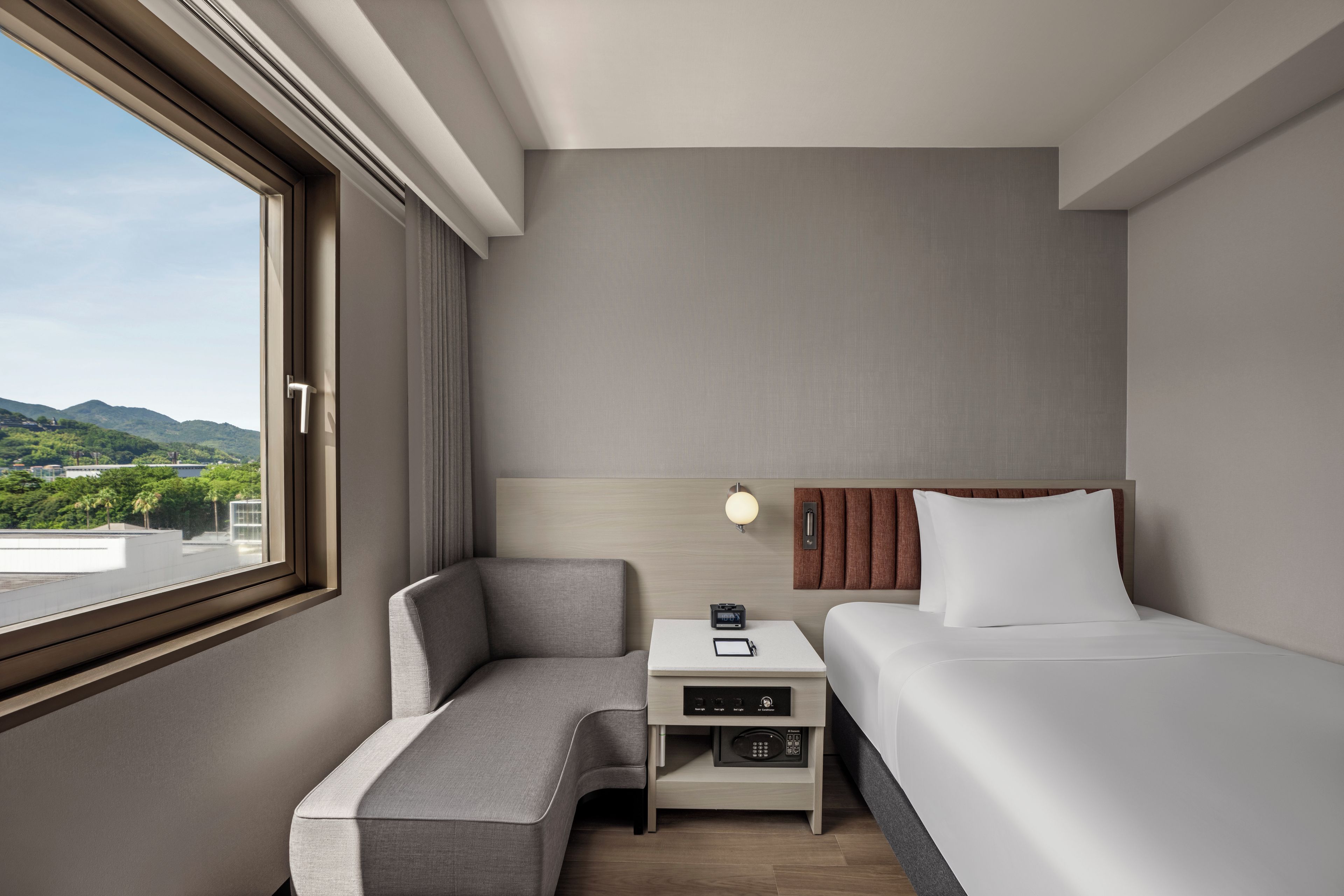 Habitación de hotel con cama, mesita de noche, una silla y vista al exterior.