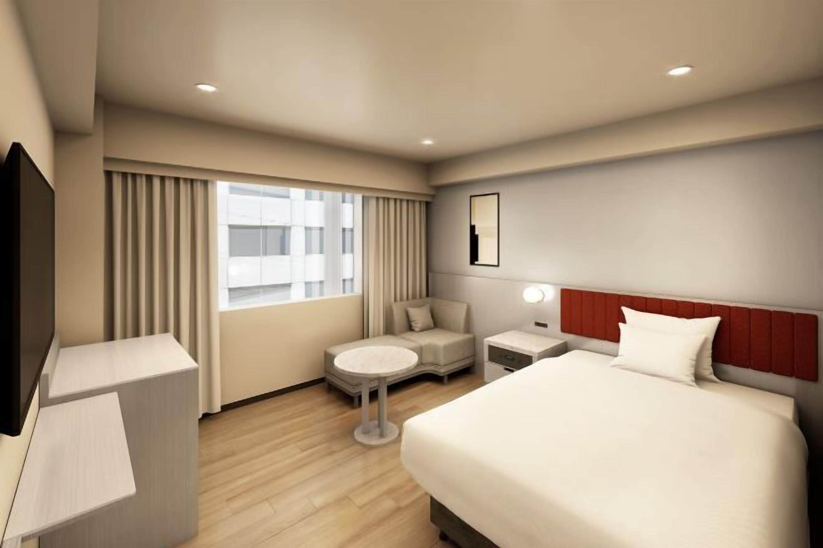 Ein Hotelzimmer mit Bett, Schreibtisch, Stuhl, kleinem Tisch, Fernseher und einem Fenster mit Vorhängen.