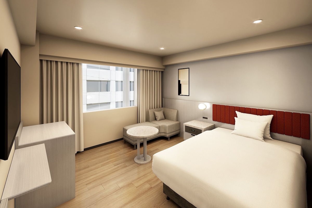 Een hotelkamer met een bed, nachtkastje, lamp en uitzicht op de stad.