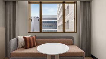 A modern living room with a sofa, a round table, and a window offering a view of a building.