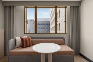 A modern living room with a sofa, a round table, and a window offering a view of a building.