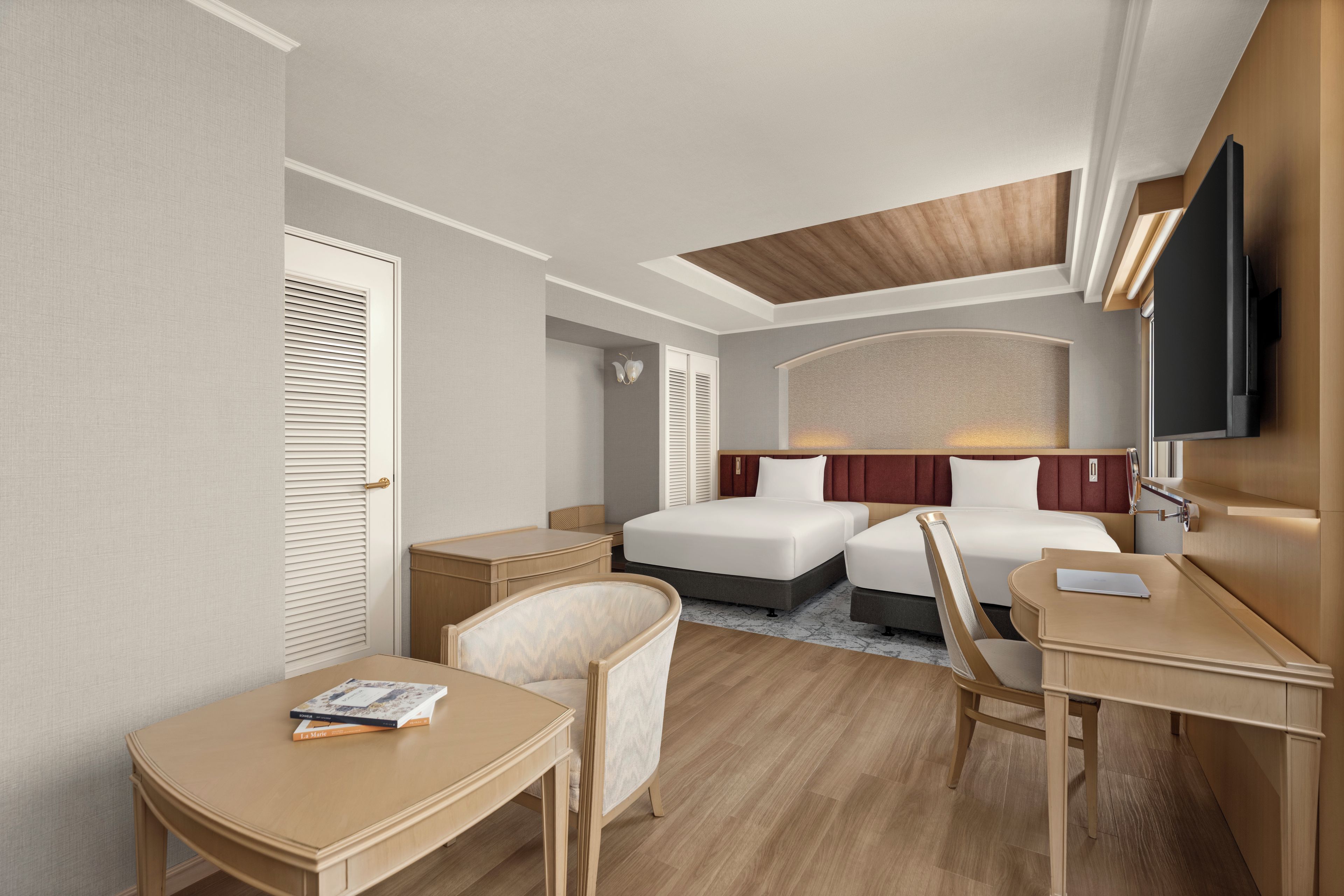 A hotel room with two beds, a desk, a chair, and a television.