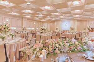 Un salón de banquetes con mesas redondas, centros de mesa florales y una araña.