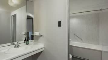 A modern bathroom with a white sink, a large mirror, a handheld showerhead, and a white toilet.