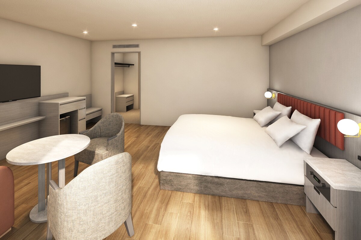 Een moderne hotelkamer met een bed, nachtkastje, stoel, televisie en een klein bureau.