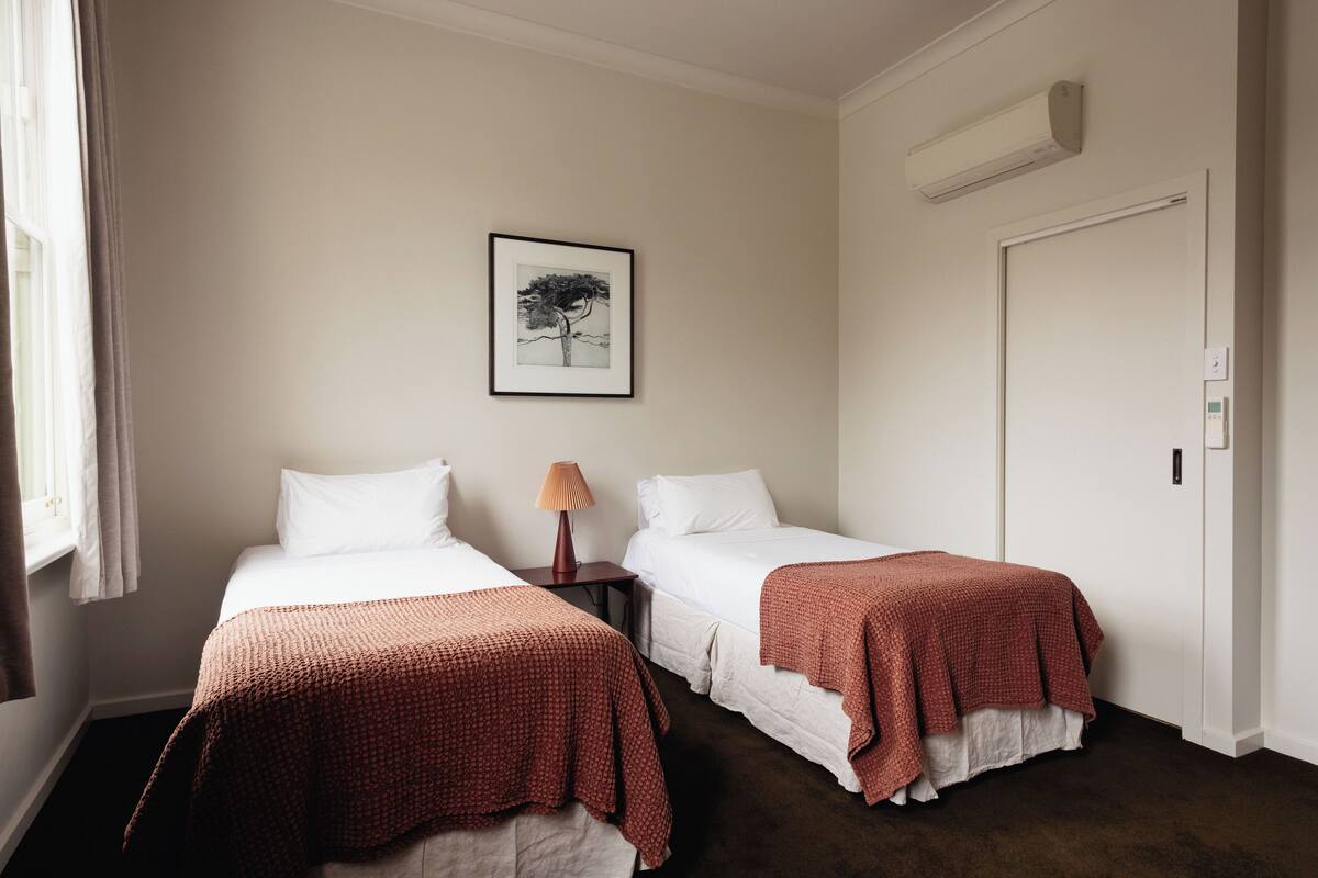 Habitación de hotel con dos camas, un cuadro enmarcado en la pared, una mesita de noche con lámpara y un equipo de aire acondicionado.