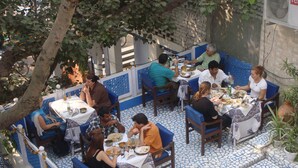 A dining area with tables and chairs, a tiled floor, and a tree providing shade. - Ray of Maya Hotel (Agra)