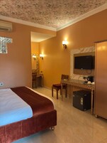 A hotel room with a bed, a desk with a television, a coffee machine, and a refrigerator.